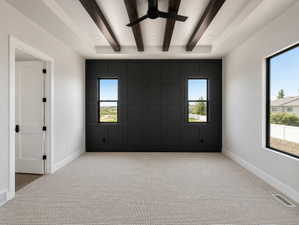 Primary bedroom featuring a dark paneled accent wall with two windows, a large window, and light-toned carpeting