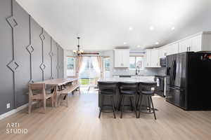 Kitchen with stainless steel appliances, hanging lights, light stone counters, light wood-style floors, and a kitchen bar