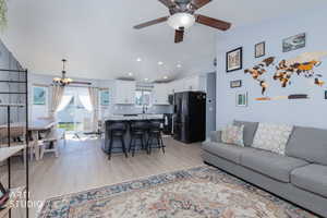 Living room with light wood-type flooring, vaulted ceiling, a chandelier, and a ceiling fan