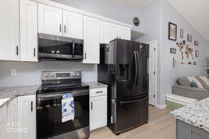 Kitchen featuring stainless steel appliances, light stone countertops, light wood-type flooring, white cabinetry, and open floor plan
