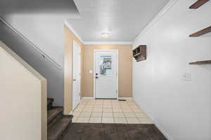 Foyer entrance with light tile patterned flooring, a textured ceiling, and crown molding