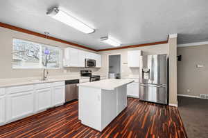 Kitchen featuring stainless steel appliances, light countertops, white cabinets, ornamental molding, and dark wood-type flooring