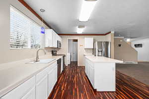 Kitchen with light countertops, stainless steel appliances, white cabinetry, a center island, and crown molding