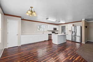 Kitchen with light countertops, stainless steel appliances, white cabinets, crown molding, and dark wood-style flooring