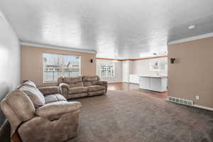 Living room featuring dark colored carpet, a textured ceiling, and ornamental molding