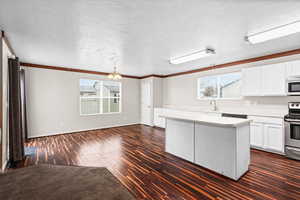 Kitchen with white cabinets, light countertops, dark wood finished floors, a center island, and a textured ceiling