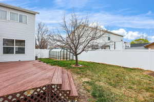 Fenced backyard featuring a greenhouse, an outbuilding, and a wooden deck