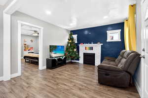 Living room with wood finished floors, a fireplace, ceiling fan, recessed lighting, and an accent wall