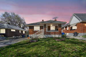 View of front facade with a front lawn, brick siding, a chimney, and a vegetable garden