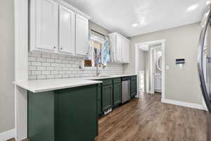 Kitchen with dual tone cabinetry, stainless steel appliances, dark wood-style flooring, tasteful backsplash, and light stone countertops