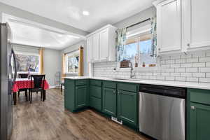 Kitchen featuring two tone cabinets, stainless steel appliances, dark wood finished floors, tasteful backsplash, and light stone counters