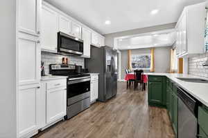 Dual tone kitchen featuring stainless steel appliances, tasteful backsplash, dual tone cabinetry, light wood-style floors, and light stone countertops