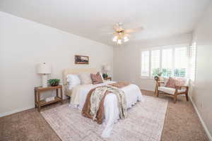 Primary bedroom with light colored carpet, louvered shutters on the corner window, and ceiling fan