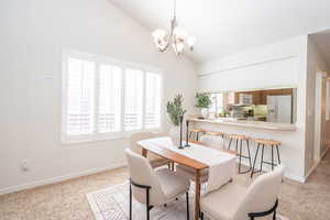 Dining area featuring lofted ceiling, light colored carpet, and louvered shutters.