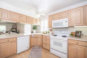 Kitchen featuring white appliances, light countertops, ceiling fan, light wood finish cabinetry, laminate flooring, and louvered shutters