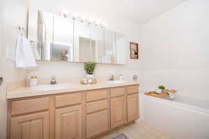 Primary bathroom featuring a Jetted tub, separate shower, and double vanity. Linoleum floors will be replaced with porcelain tile at the end of March.