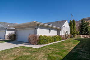 View of side of property with stucco siding, a lawn, concrete driveway, a garage. Garage faces west.