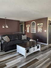 Living room featuring wood finished floors, suspended lighting, and a textured ceiling
