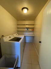 Laundry room featuring a textured ceiling, light tile patterned flooring, and washing machine and dryer