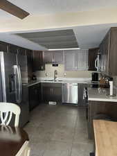 Kitchen with dark wood finish cabinetry, stainless steel appliances, a textured ceiling, and light tile patterned floors
