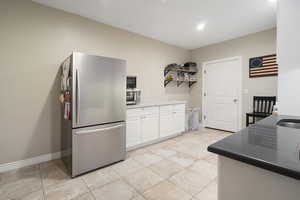 Kitchen with freestanding refrigerator, white cabinetry, open shelves, and light tile patterned floors