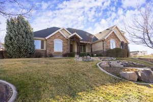 Ranch-style home with a front yard, roof with shingles, and stone siding
