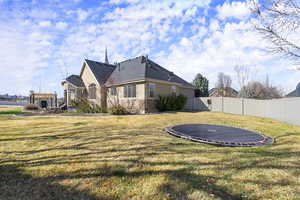 Rear view of house featuring stucco siding, a fenced backyard, roof with shingles, and a trampoline