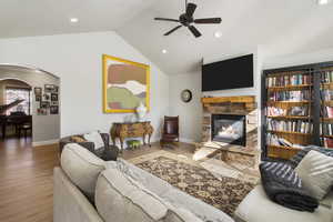 Living room featuring wood finished floors, ceiling fan, arched walkways, a fireplace, and recessed lighting