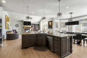 Kitchen featuring an island with sink, a ceiling fan, stainless steel appliances, open floor plan, and light wood-type flooring