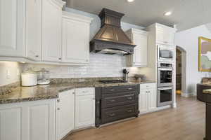 Kitchen with white cabinetry, a textured ceiling, dark stone counters, stainless steel appliances, and light wood-style floors