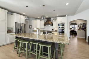 Kitchen with arched walkways, stainless steel appliances, a kitchen bar, light wood finished floors, and a textured ceiling