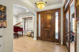 Foyer with light wood-style floors, ornamental molding, and arched walkways