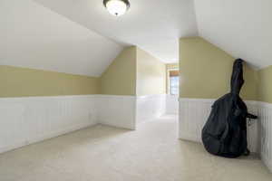 Bonus room with a wainscoted wall, a textured ceiling, and light colored carpet