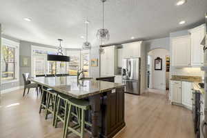 Two tone kitchen featuring arched walkways, a breakfast bar area, dual tone cabinets, a spacious island, and light wood-style floors