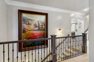 Corridor featuring crown molding, arched walkways, and an upstairs landing