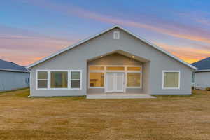 Back of house at dusk with a patio, stucco siding, a lawn, and french doors