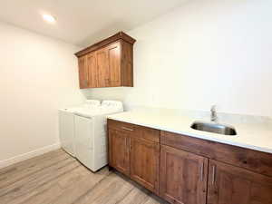 Laundry area featuring light wood-type flooring, separate washer and dryer, and cabinet space