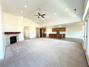 Unfurnished living room featuring light colored carpet, a premium fireplace, a ceiling fan, vaulted ceiling, and recessed lighting