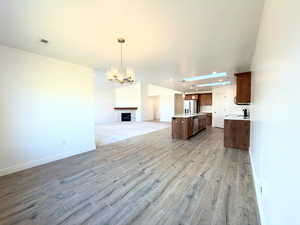 Kitchen featuring open floor plan, a center island with sink, hanging lights, a fireplace, and stainless steel appliances