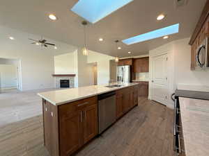 Kitchen featuring a skylight, stainless steel appliances, a tiled fireplace, decorative light fixtures, and an island with sink