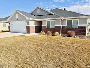 View of front of house with a front lawn, brick siding, a garage, and stucco siding