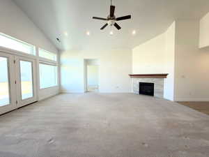 Unfurnished living room with ceiling fan, a tiled fireplace, lofted ceiling, recessed lighting, and light colored carpet