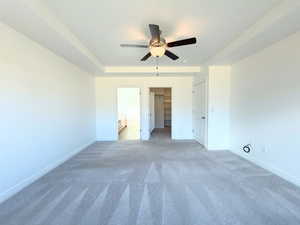 Unfurnished bedroom featuring connected bathroom, a spacious closet, carpet floors, a ceiling fan, and a tray ceiling