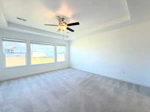 Carpeted empty room featuring a tray ceiling and ceiling fan