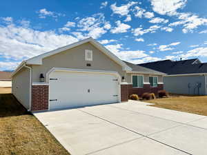 Ranch-style home featuring brick siding, concrete driveway, an attached garage, a front yard, and stucco siding