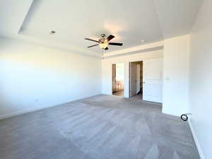 Unfurnished bedroom featuring ensuite bath, light colored carpet, a ceiling fan, and a raised ceiling