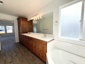 Bathroom featuring double vanity, dark wood-type flooring, and a garden tub
