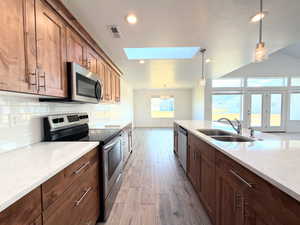 Kitchen with a skylight, stainless steel appliances, decorative light fixtures, light stone counters, and lofted ceiling