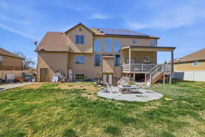 Rear view of property with a patio area, roof mounted solar panels, stucco siding, a fire pit, and a wooden deck