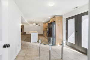 Kitchen with light wood finish cabinetry, black fridge with ice dispenser, recessed lighting, light tile patterned floors, and a fireplace